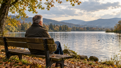 Ein Mann sitzt auf einer Bank am See und blickt auf das Wasser in herbstlicher Landschaft.